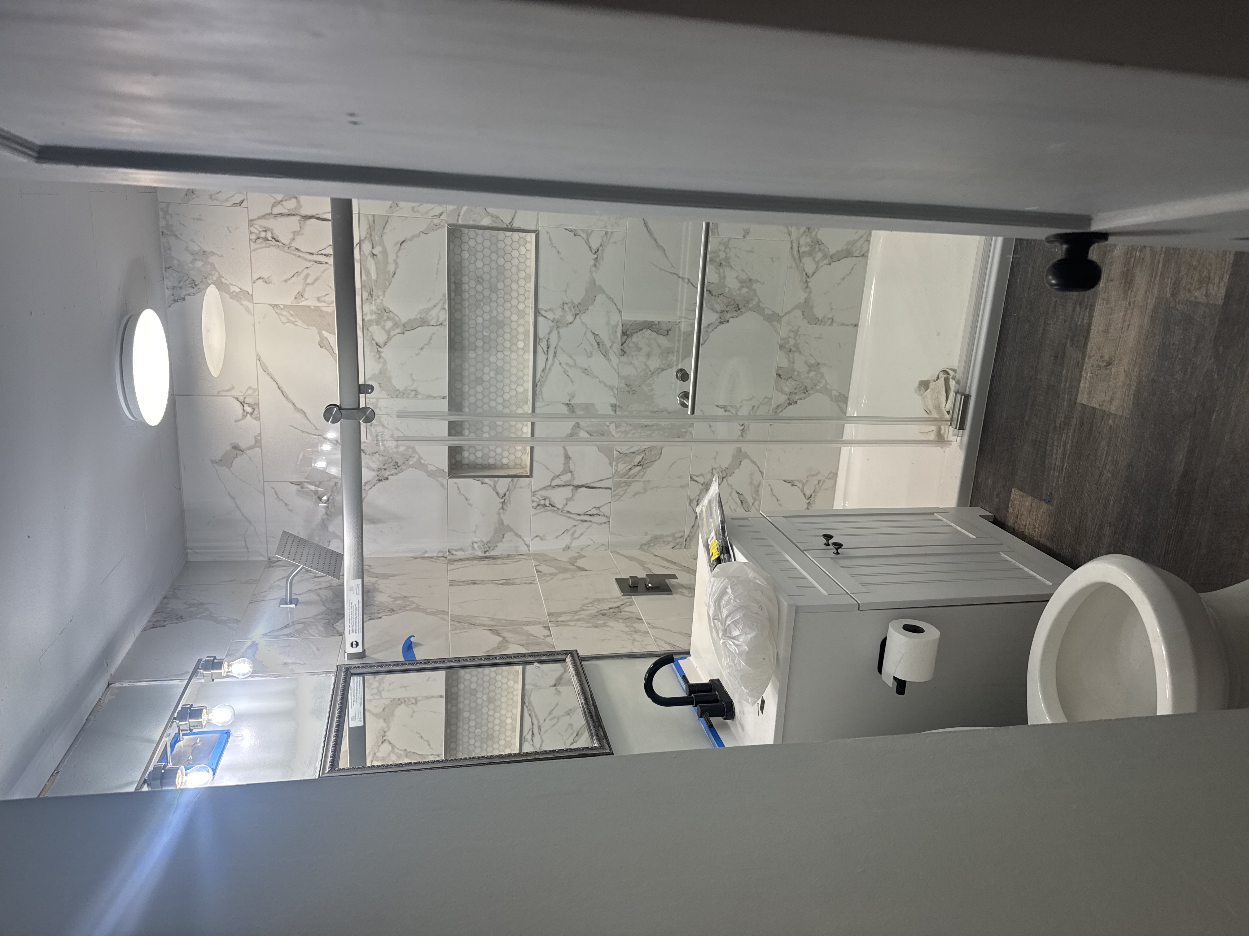 After — floor-to-ceiling marble tile, glass shower enclosure, hexagon niche